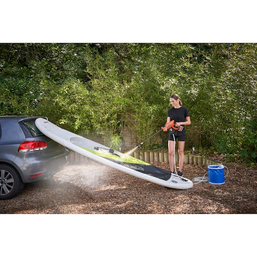 BLACKDECKER BZOIHK2 portable pressure washer cleaning stand up paddle board outdoors next to car.