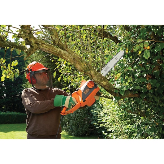 BLACKDECKER CS2040 chainsaw used outdoors for cutting tree branches, visible orange body and blade.