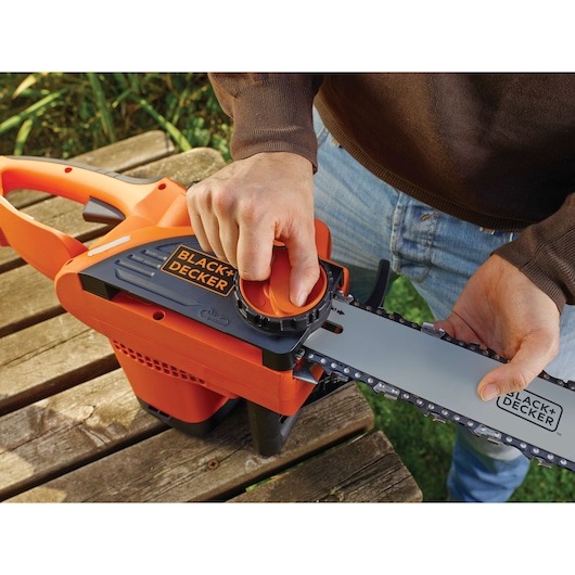 BLACK+DECKER CS2040 chainsaw close-up, user adjusting chain tension with hand, outdoor setting.