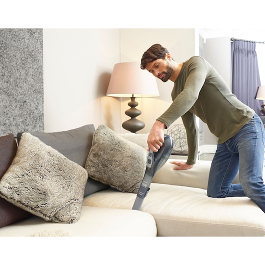 BLACKDECKER DVA320J handheld vacuum used to clean beige sofa cushions in a living room.
