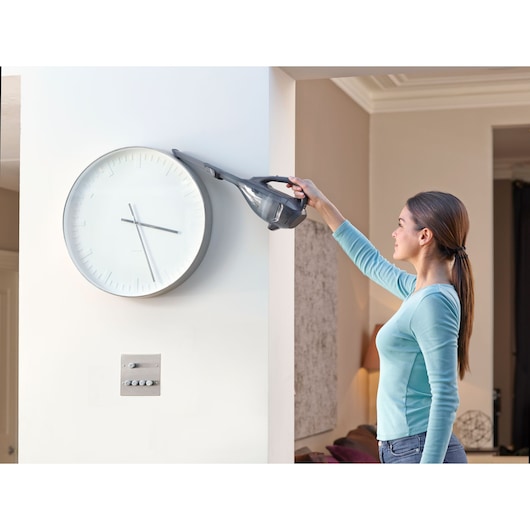 BLACKDECKER DVA320J handheld vacuum used to clean above a wall clock in a modern living room.