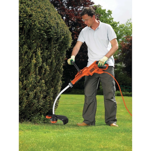 BLACKDECKER GL7033 orange electric grass trimmer used outdoors for edging lawn near shrubs.