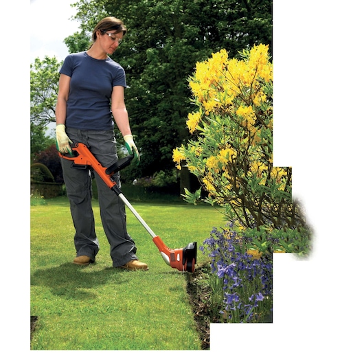 Photo of BLACKDECKER GLC1823L20 grass trimmer in use, orange and black, trimming lawn edge near flowers.