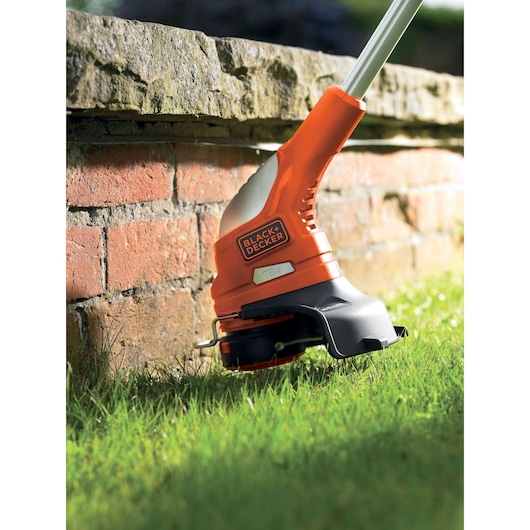 BLACK+DECKER GLC1823L20 grass trimmer close-up trimming lawn edge near brick wall.
