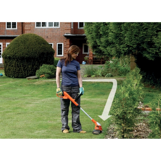 BLACKDECKER GLC1823L20 cordless grass trimmer held by a person on a garden lawn near hedge.