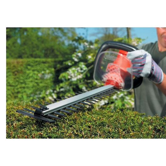Photo of BLACKDECKER GT7030 hedge trimmer in use, cutting green foliage outdoors.