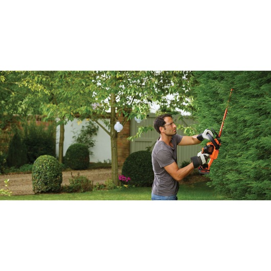 BLACKDECKER hedge trimmer GTC18504PC in use, orange and black tool trimming green hedge outdoors.
