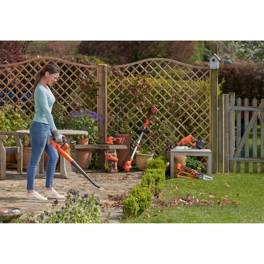 BLACKDECKER GWC1820PC cordless leaf blower in use outdoors, orange and black design, garden setting.