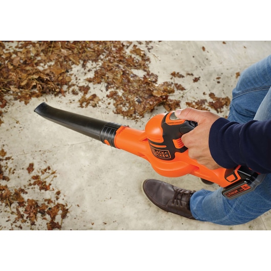 BLACKDECKER GWC1820PC cordless leaf blower in use, orange design clearing dry leaves.