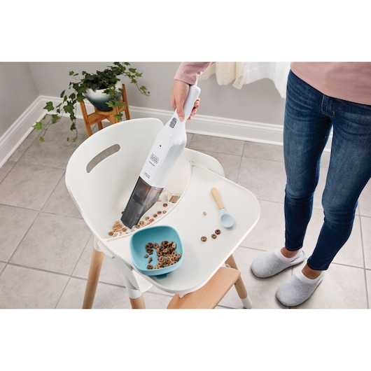 BLACK+DECKER HLVC315B11 handheld vacuum cleaning cereal on a white high chair tray, indoor photography, top view.