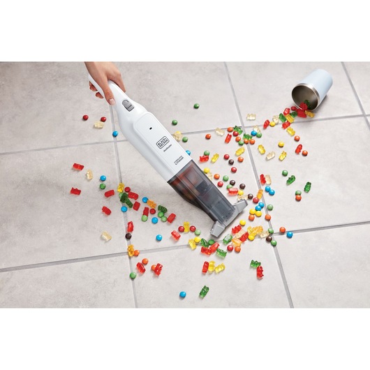 Photo of BLACK+DECKER HLVC315B11 handheld vacuum cleaning colorful candy from tiled floor, top view.