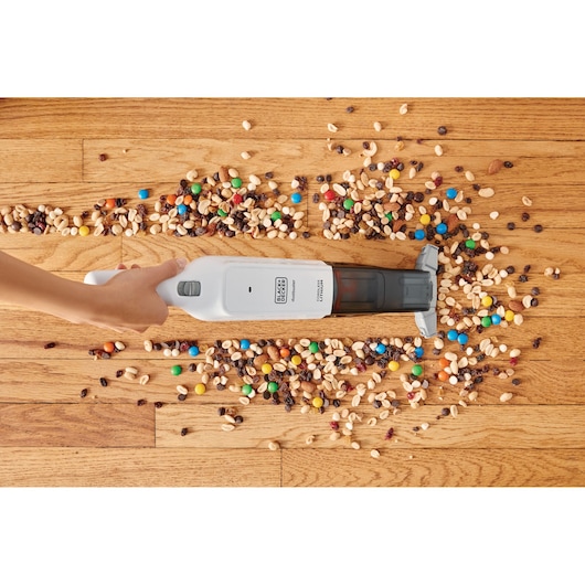 BLACK+DECKER HLVC315B11 handheld vacuum cleaning mixed snacks from hardwood floor, top view.