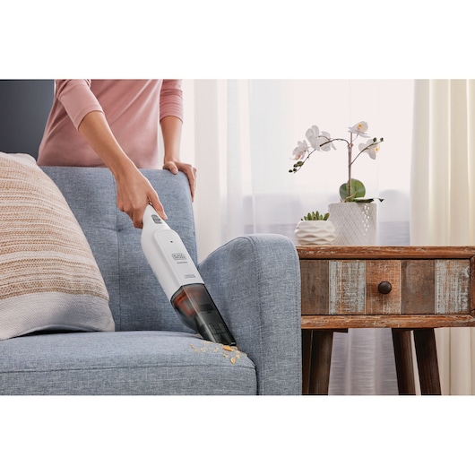 BLACKDECKER HLVC315J11 handheld vacuum cleaning sofa crumbs in living room setting.