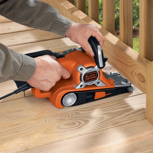 BLACKDECKER KA88 belt sander in use sanding wooden decking, orange and black design, product photography.