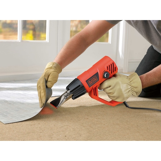BLACKDECKER KX2001K heat gun used for lifting flooring, orange body, gloved hand, product in action.