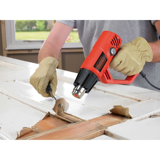 BLACKDECKER KX2001K heat gun used to strip paint from wood door, close-up with gloved hands.