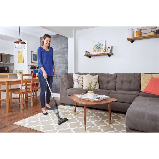 BLACKDECKER NSVA315J stick vacuum cleaner used on living room rug near sofa and coffee table.