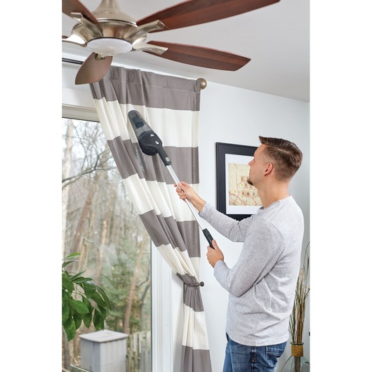 Photo of BLACKDECKER NSVA315J handheld vacuum with extension being used to clean ceiling fan blades.