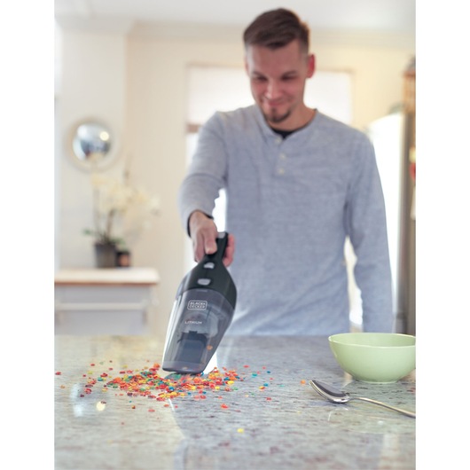 BLACKDECKER NSVA315J handheld vacuum cleaning colorful crumbs on kitchen counter near green bowl and spoon