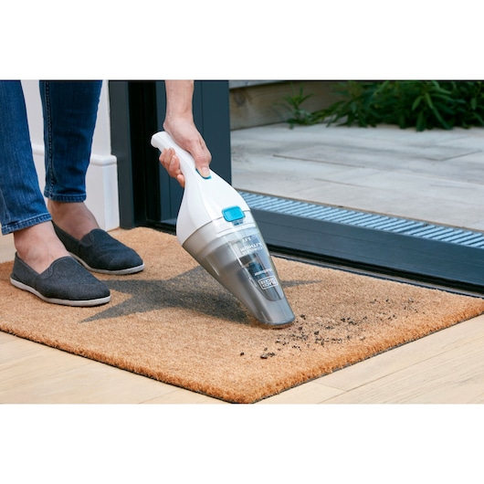 BLACKDECKER NVC115JL handheld vacuum cleaning debris from a brown doormat near an open door.