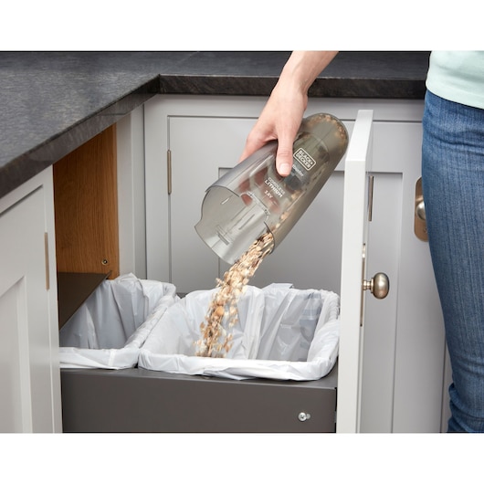 Photo of BLACK+DECKER NVC115JL handheld vacuum being emptied over kitchen trash bin, debris falling out.