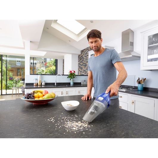 BLACKDECKER NVC115WA handheld vacuum cleaning countertop crumbs in kitchen near bowl of fruit.