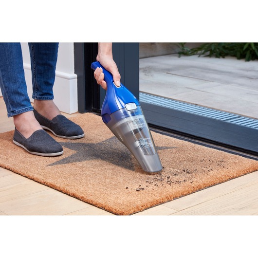 BLACK+DECKER NVC115WA handheld vacuum cleaning dirt from a doormat near a door, SKU NVC115WA.