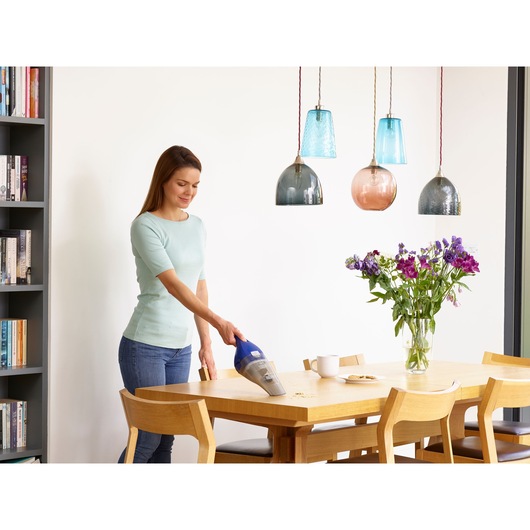 BLACKDECKER NVC115WA handheld vacuum cleaning crumbs on dining table in modern kitchen setting.