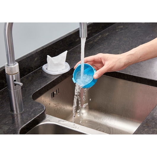 BLACKDECKER NVC215WA blue vacuum filter being rinsed under running water in a kitchen sink, side angle.