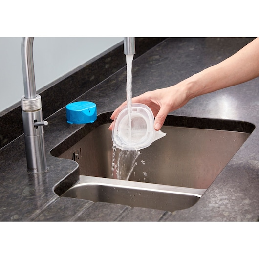 Photo of cleaning BLACKDECKER NVC215WA vacuum filter under running water in a kitchen sink.