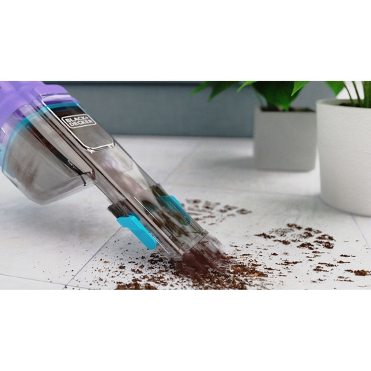 BLACK+DECKER NVD220BP handheld vacuum cleaning dirt from white floor with potted plants in background.