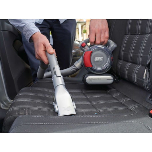 Photo of BLACKDECKER PD1200AV handheld vacuum cleaning a car seat, showing hose attachment and compact design.