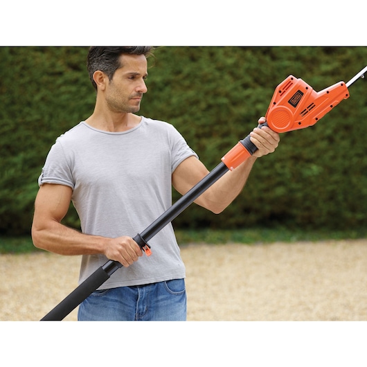 BLACKDECKER PH5551 pole hedge trimmer held outdoors, orange casing and adjustable black pole.