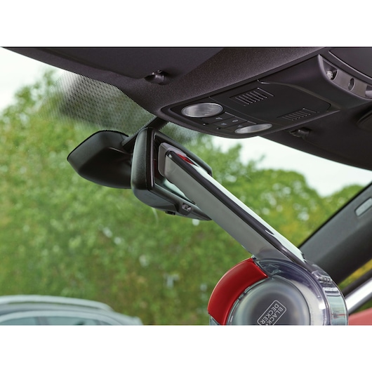 A BLACK+DECKER handheld vacuum cleaner (model PV1200AV) is being used to clean a car interior, targeting the area around the rearview mirror and windshield.