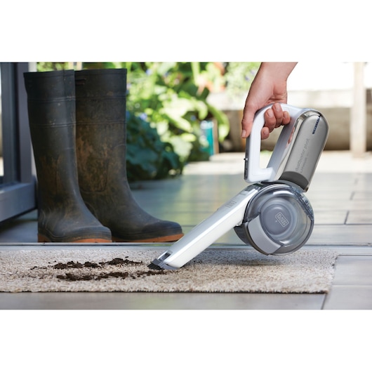 BLACKDECKER PV1820L handheld vacuum cleaning dirt from carpet near muddy boots, outdoor setting.