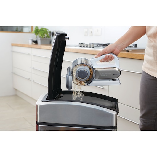 BLACKDECKER PV1820L handheld vacuum being emptied into a trash can in a modern kitchen, side view.