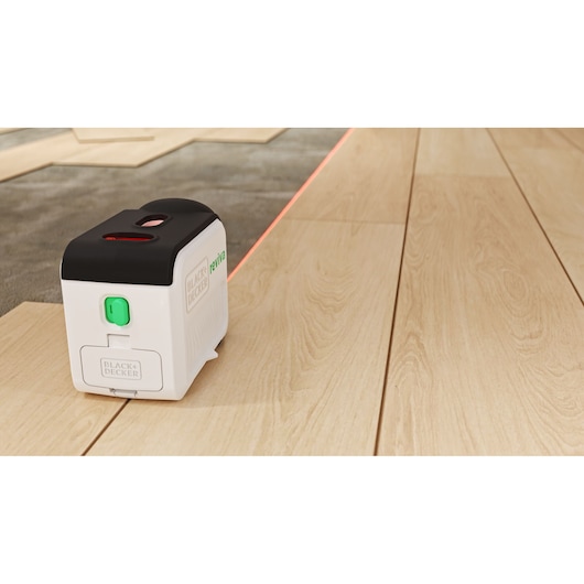 BLACKDECKER REVBDLL100 laser level on wooden floor projecting a straight red laser line, perspective view.