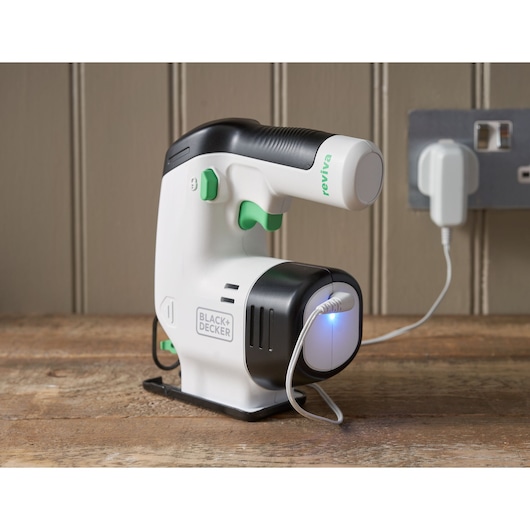 BLACK+DECKER REVJ12C handheld white and black fabric care device with green accents charging on wooden surface.