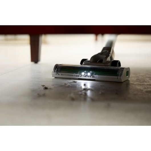 BLACKDECKER REVSV18D1 vacuum with LED lights cleaning under furniture, low-angle view, collecting dust and debris.