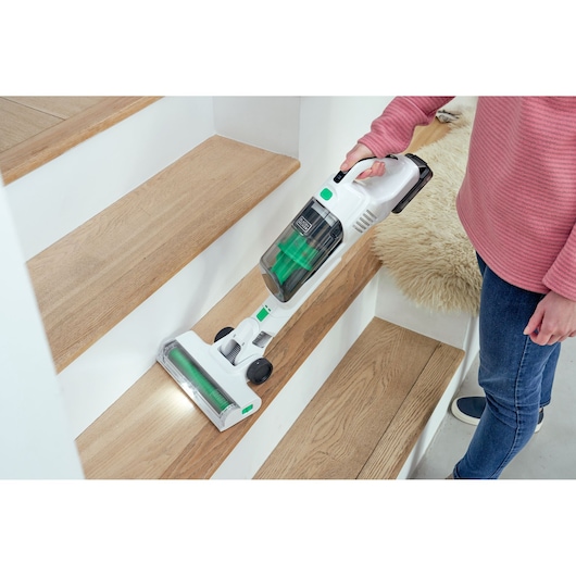 BLACKDECKER REVSV18D1 cordless stick vacuum with green accents cleaning wooden stairs.