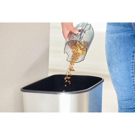 BLACKDECKER REVSV18D1 vacuum dust container being emptied into a metal trash bin, close-up view.