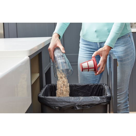 Photo of a person emptying BLACK+DECKER SVB620JW vacuum canister with filter into kitchen trash bin.