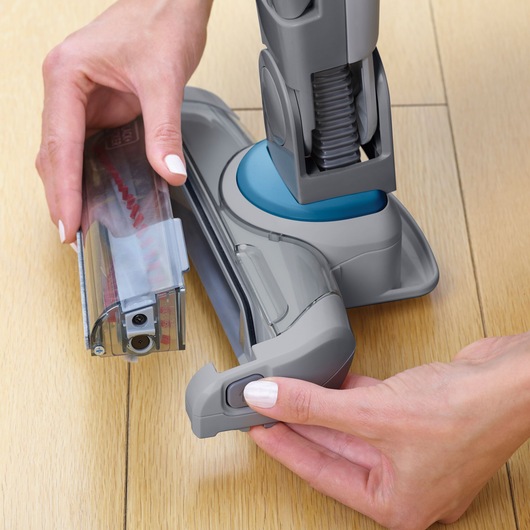 BLACKDECKER SVJ520BFS vacuum cleaner brush head removal on light wood floor, close-up angle.