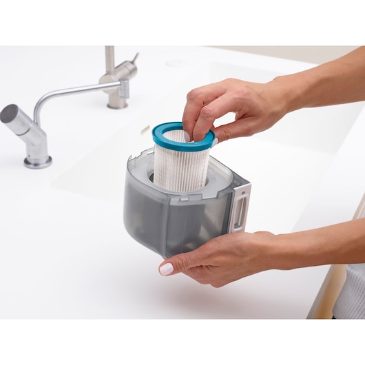 BLACKDECKER VPFE20 vacuum filter being removed from dust container near a white sink.