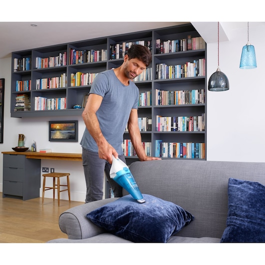 BLACKDECKER WDC115WA handheld vacuum cleaning a blue cushion on a grey sofa in a modern living room.