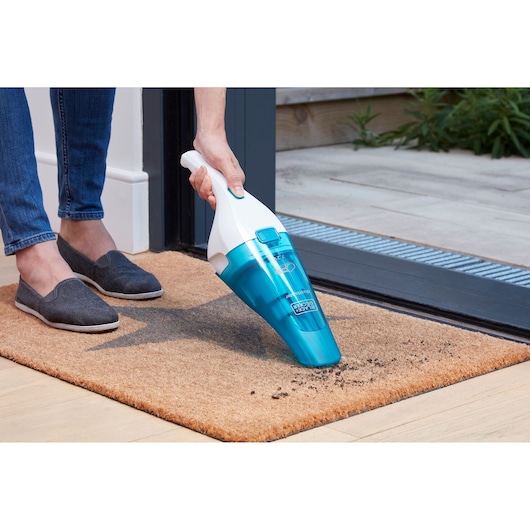 BLACKDECKER WDC115WA handheld vacuum cleaning dirt from a doormat near a doorway.