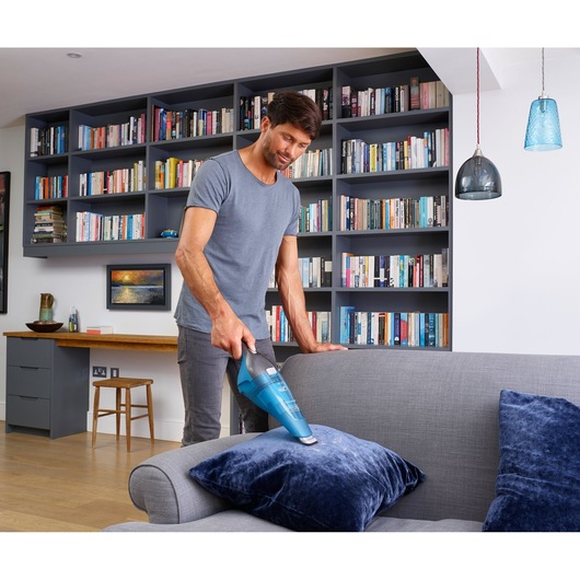 BLACK+DECKER WDC215WA handheld vacuum cleaning blue pillow on grey sofa in modern living room.