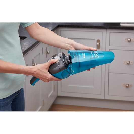BLACKDECKER WDC215WA blue handheld vacuum cleaner held in kitchen, showing dust container removal.